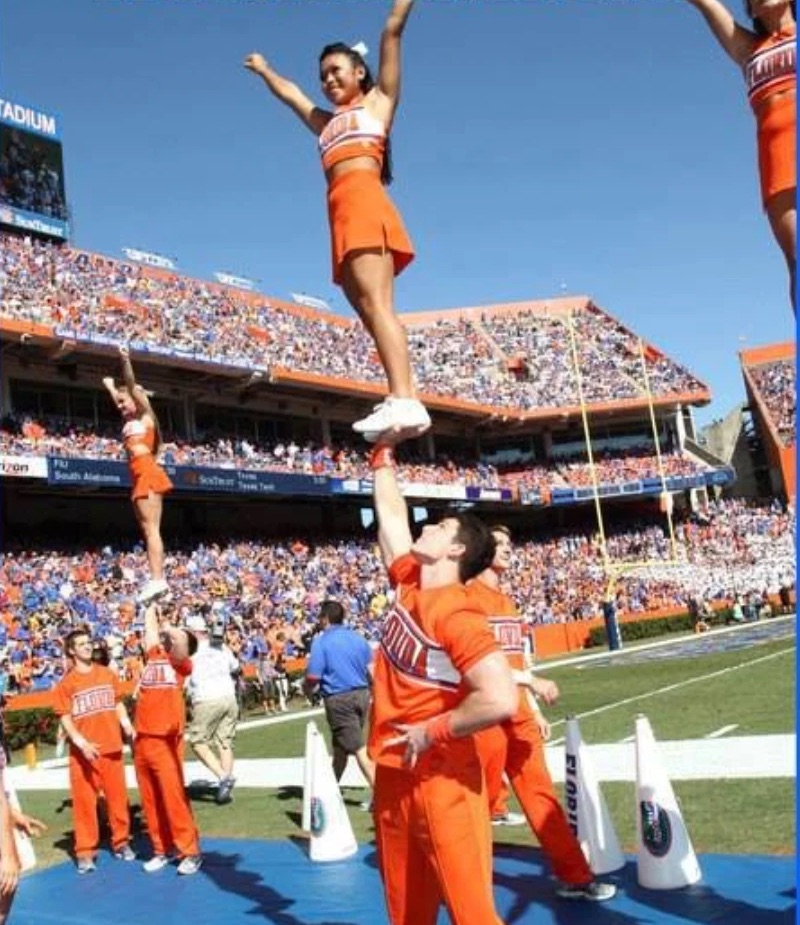 Ben Sunter holding a cheerleader overhead on one arm during a game at Ben Hill Griffin Stadium